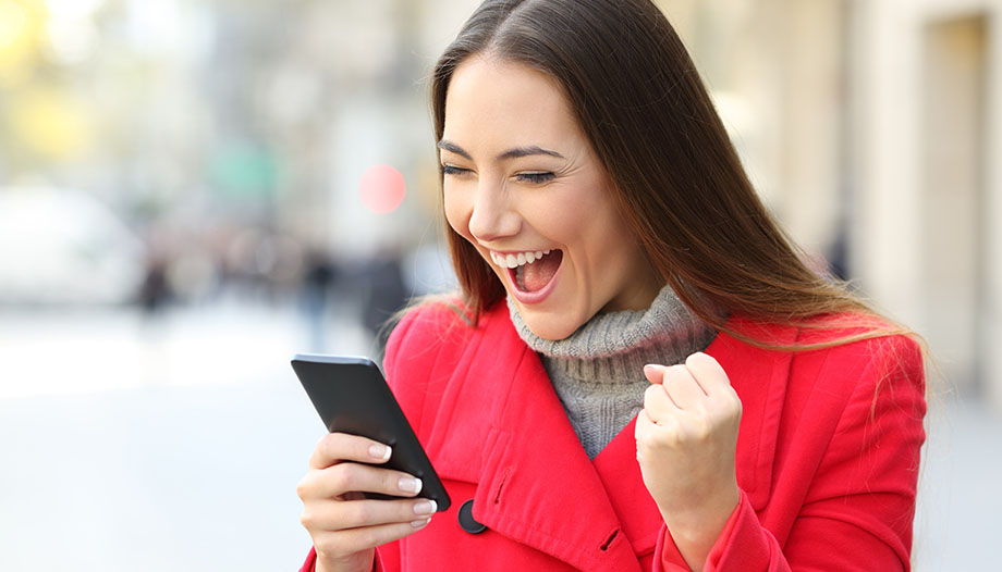 woman pumping her fist in celebration with her mouth open in excitement while looking at her cell phone